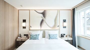 A modern hotel room with a large bed, bedside tables, a desk, and a view of the city through the window.