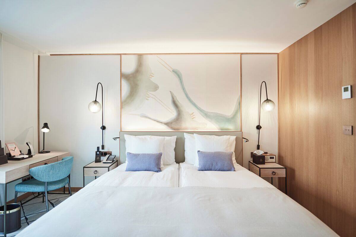 A modern hotel room with a large bed, two bedside tables, a desk, and a chair.