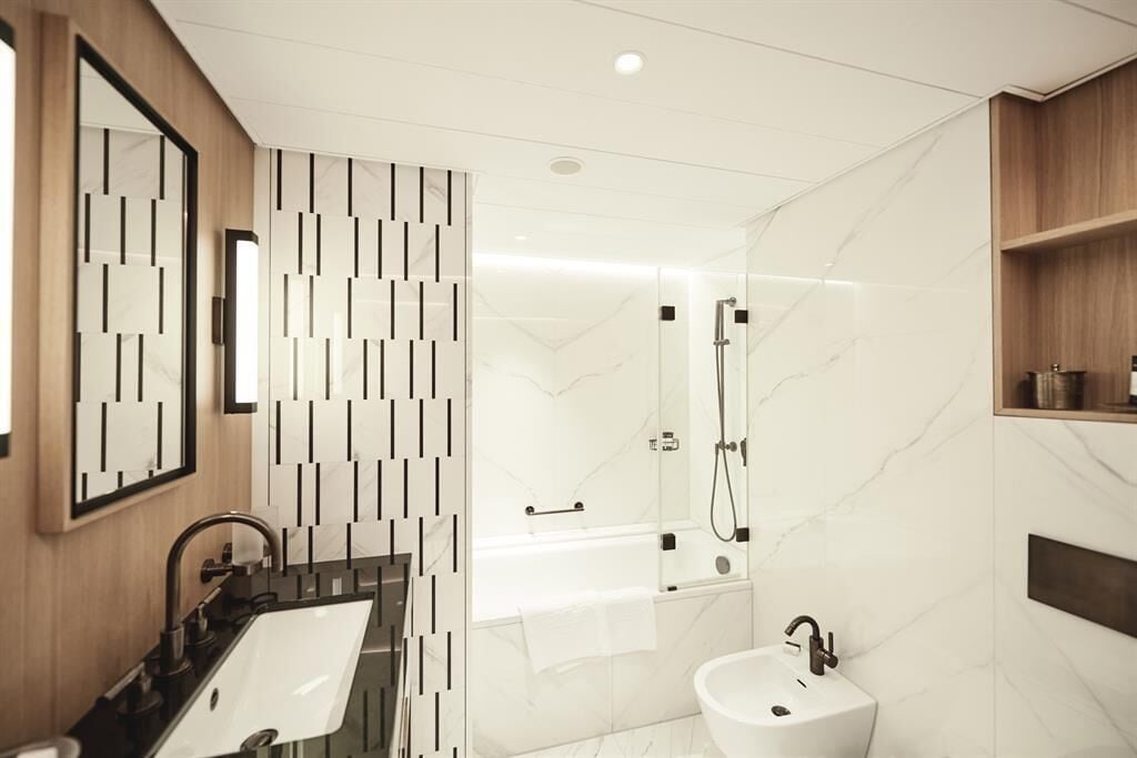 Un bagno moderno con lavandino nero, mobile bagno bianco, cabina doccia in vetro e parete rivestita in marmo.