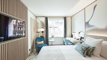 A hotel room with a bed, a desk, a chair, a TV, and a window with a view of buildings.
