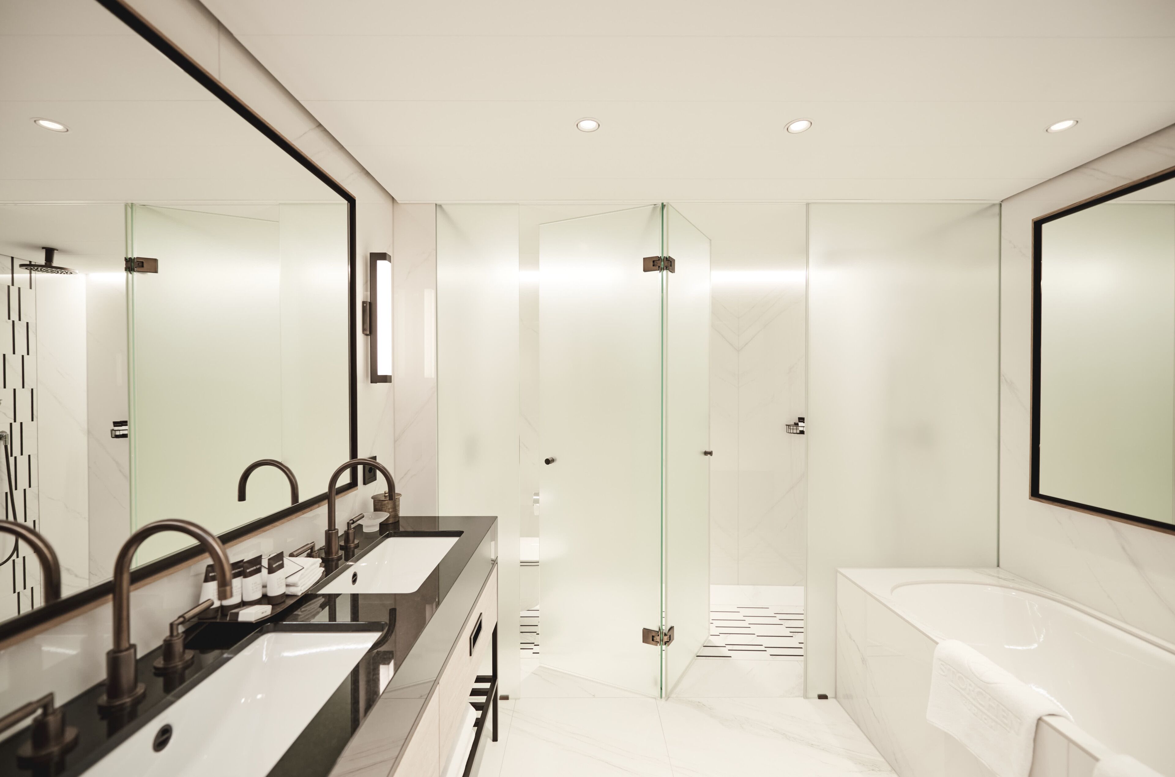 A modern bathroom with a glass-enclosed shower, a large mirror, and a bathtub.