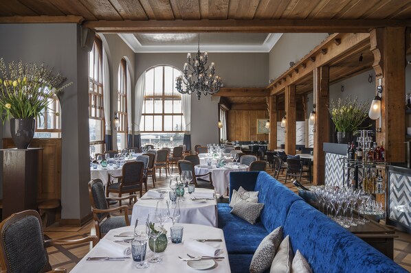 Un comedor con mesas redondas, sofás azules y una zona de bar con botellas.