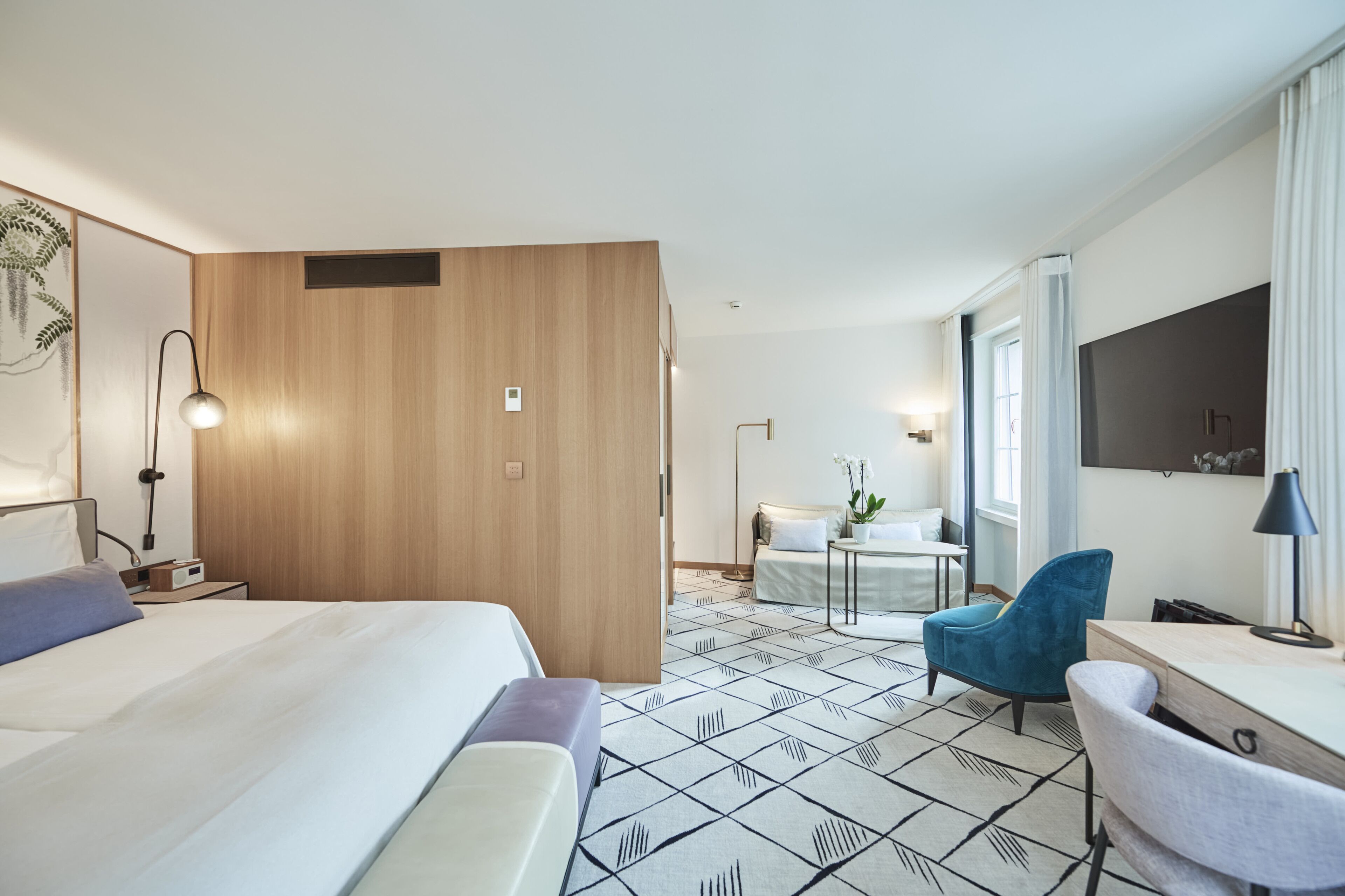 Une chambre d’hôtel avec un lit, un bureau, une chaise, une petite table et une fenêtre.