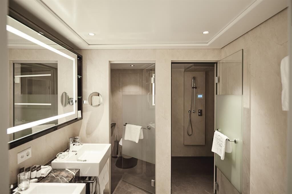 Een moderne badkamer met een grote spiegel, twee wastafels, een douche en een douchecel met glazen wanden.
