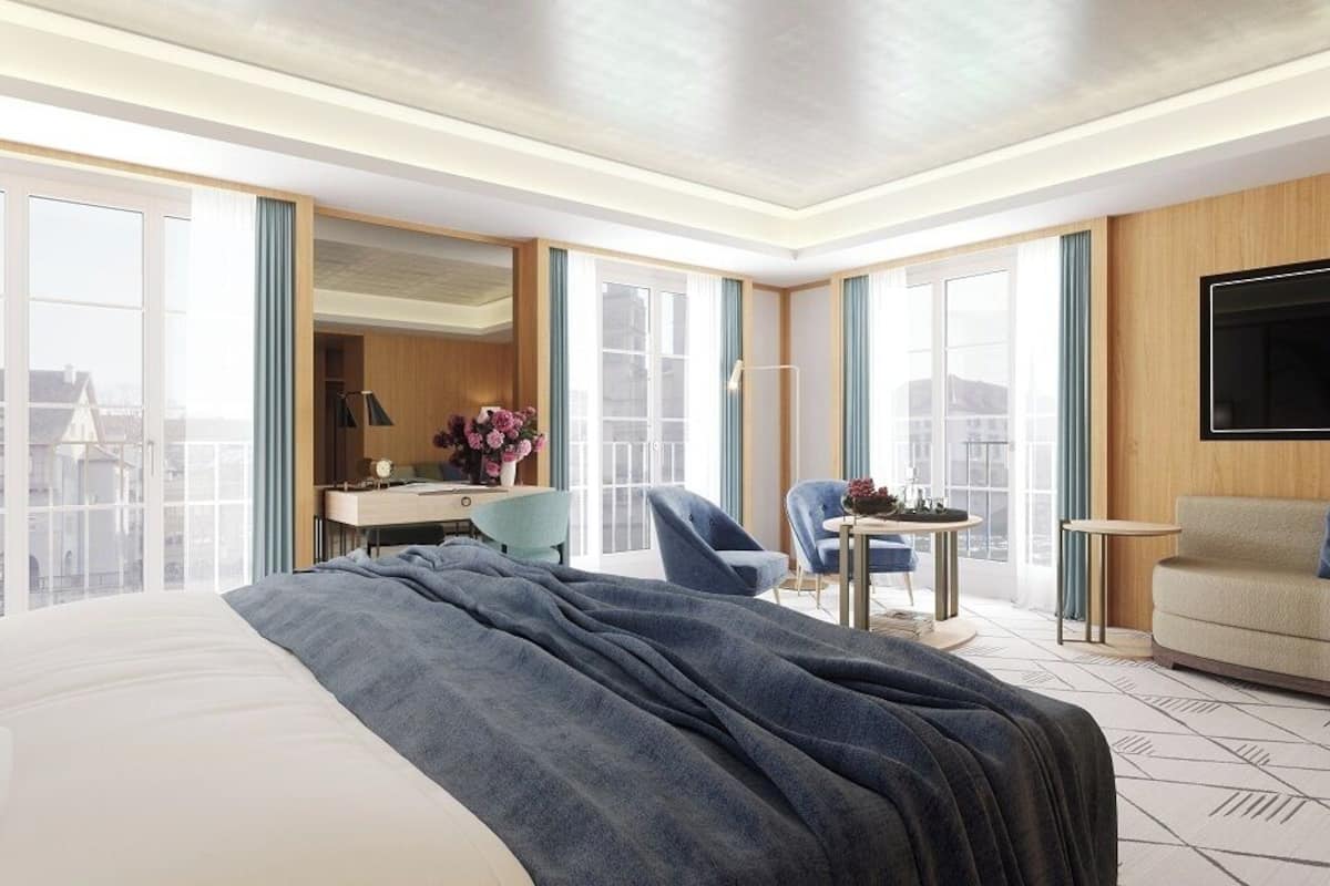 A hotel room with a large bed, a desk, a chair, a sofa, and a TV.