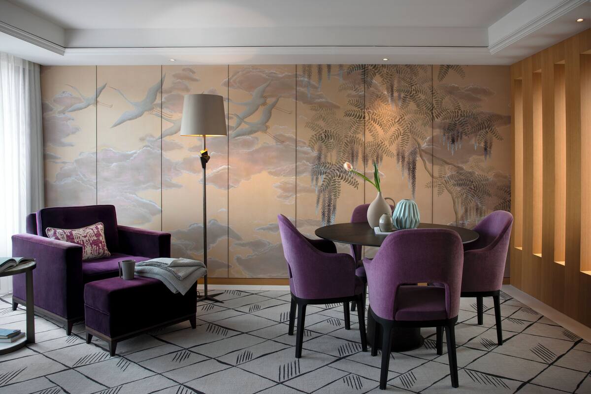 A modern room with a large wall mural, a round table with purple chairs, and a purple armchair.