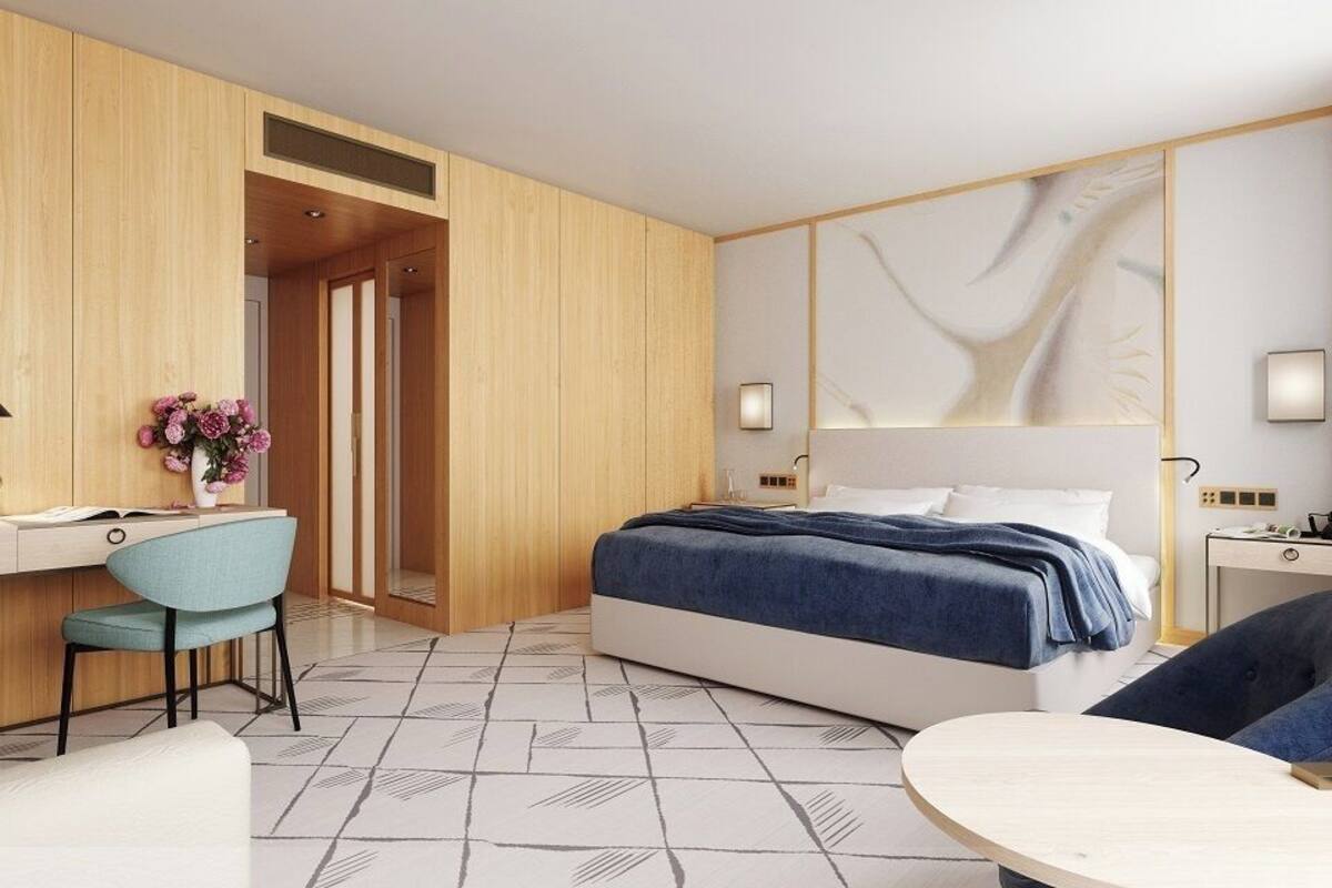 A modern hotel room with a bed, desk, chair, and a small table.