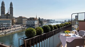 A terrace with a table set for dining, overlooking a river with buildings and a bridge in the background.