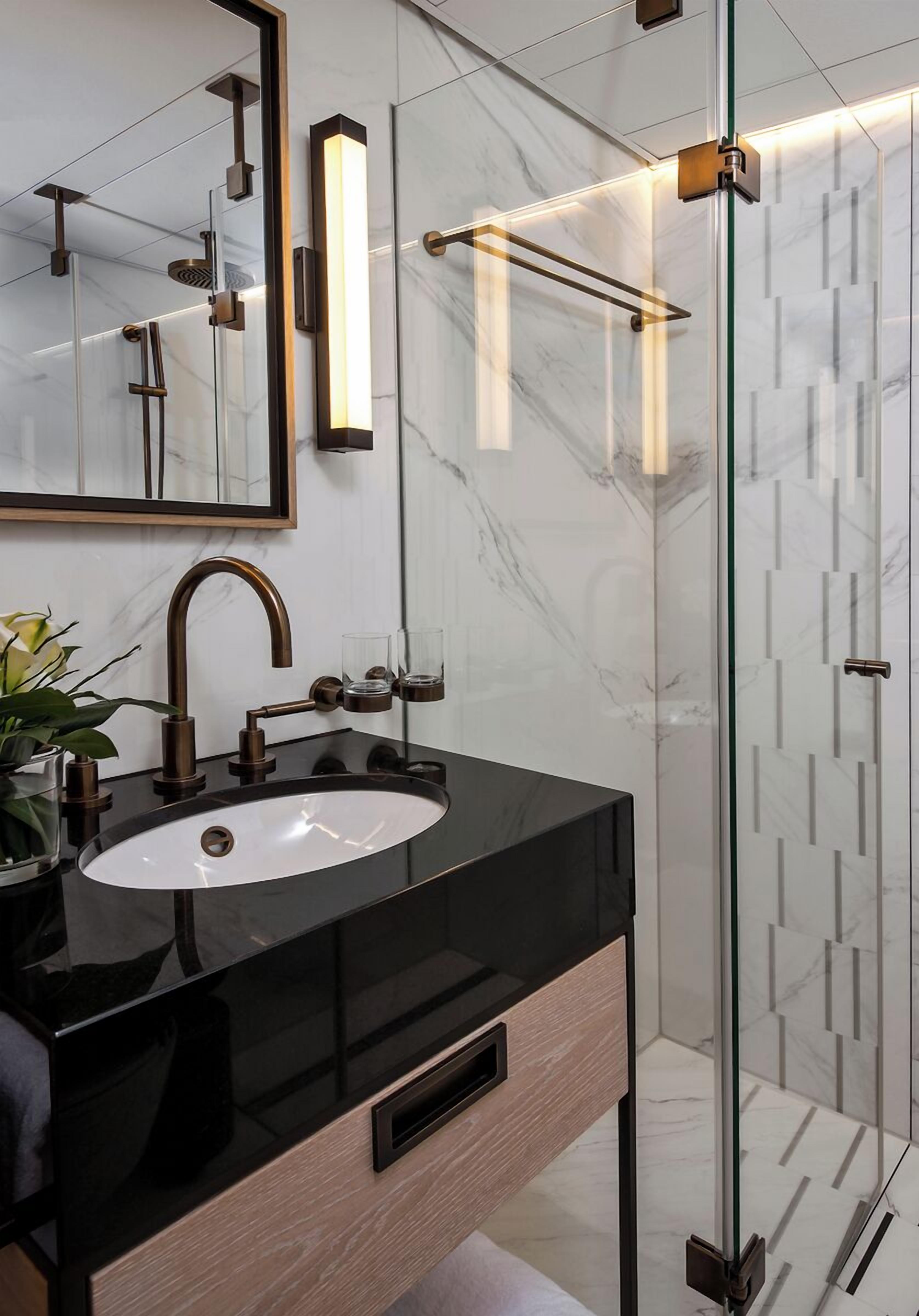 Un baño moderno con encimera negra, lavabo blanco, espejo grande y cabina de ducha con paredes de vidrio.