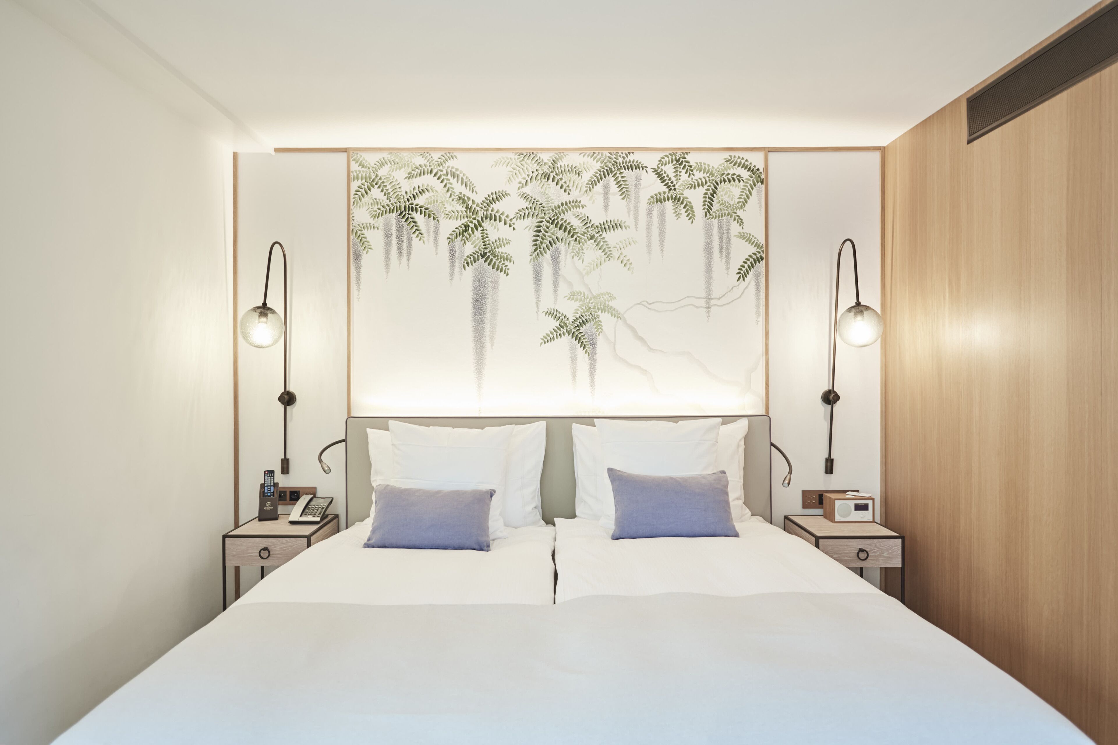 A modern bedroom with a large bed, two bedside tables, a wall-mounted lamp, and a decorative headboard.
