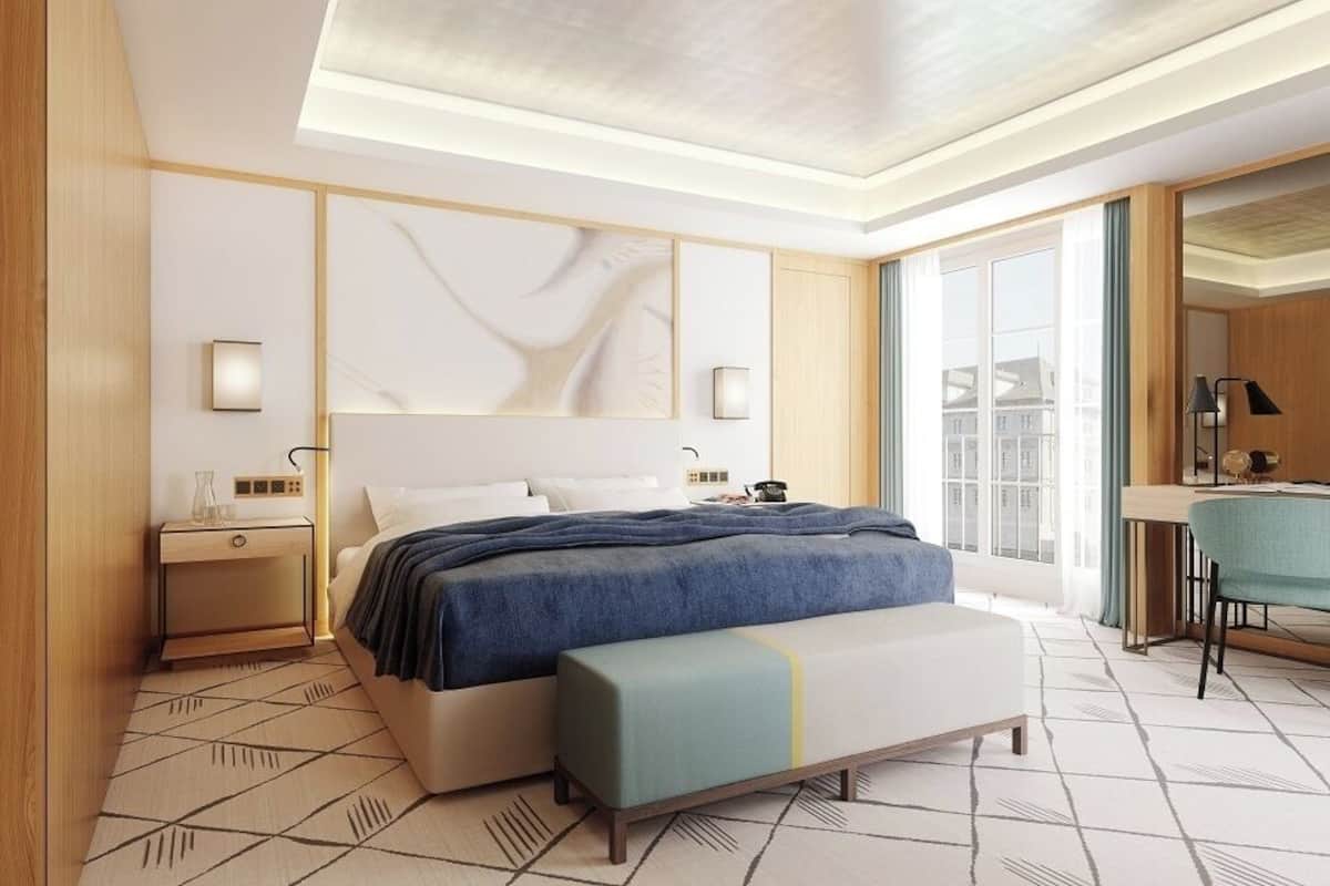 A modern hotel room with a large bed, bedside tables, a desk, and a view of the city.