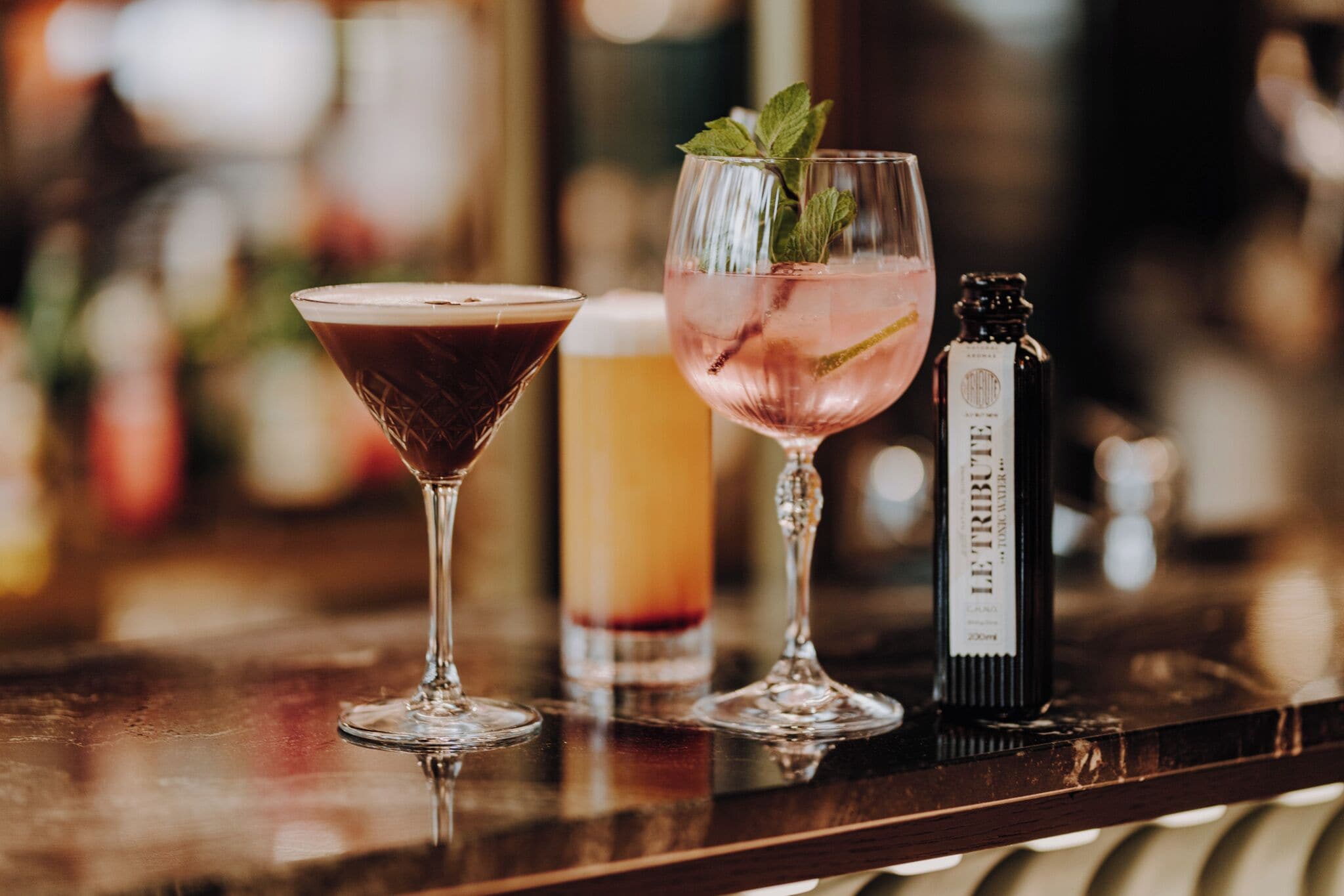 A bar setting with two glasses of cocktails and a bottle of liquor.