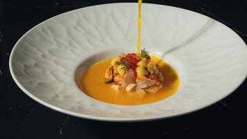 A hand pouring a yellow sauce onto a white plate with a seafood dish.