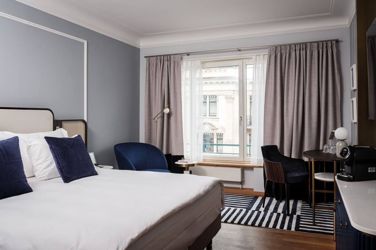 Habitación de hotel con cama, escritorio, silla, cafetera y vista a la ciudad por la ventana.