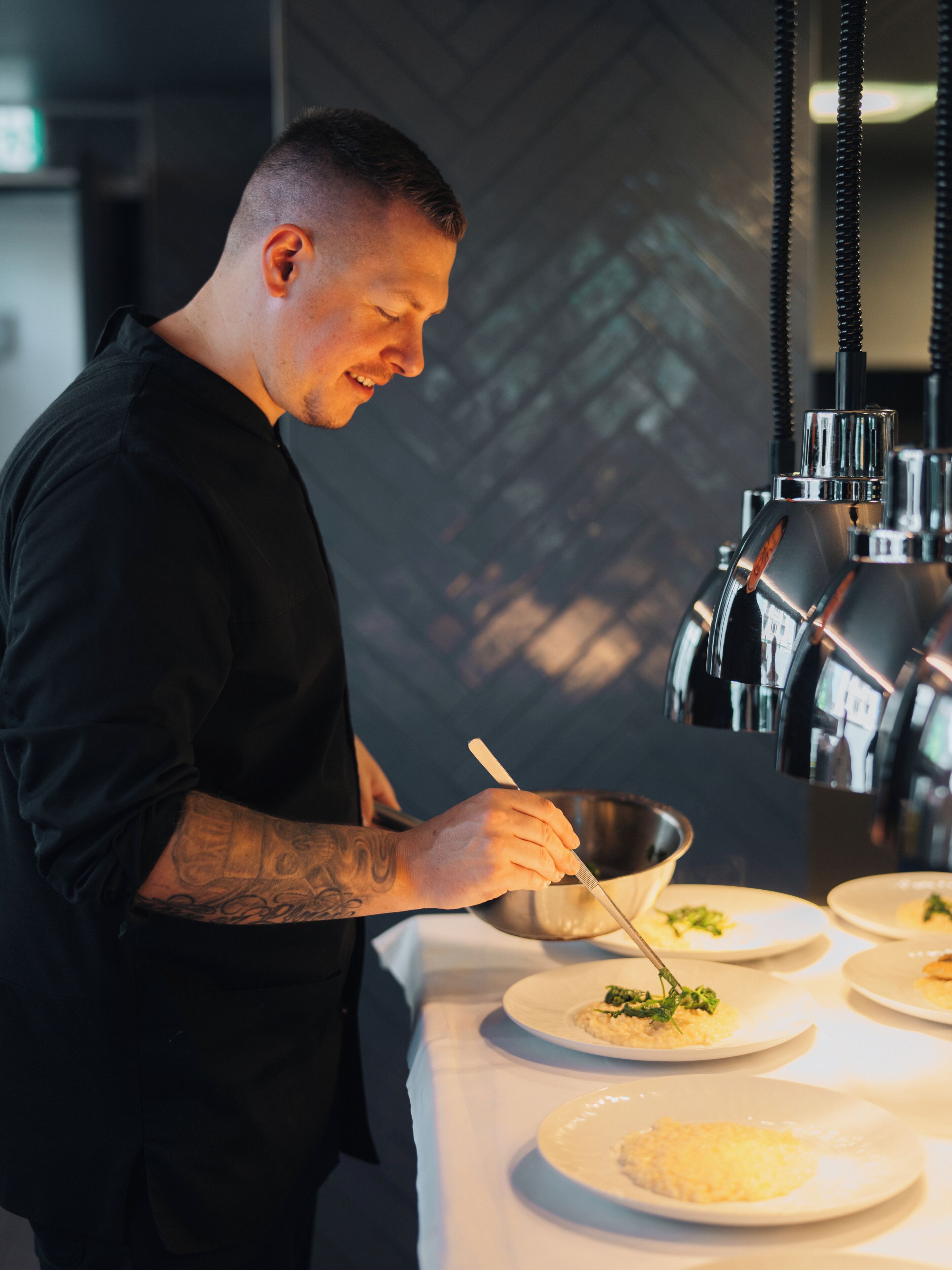 A chef in a black uniform preparing food in a kitchen with stainless steel appliances and a white countertop.