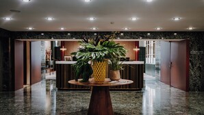 Eine moderne Lobby mit einem zentralen Holztisch, Zimmerpflanzen und einer Rezeption.