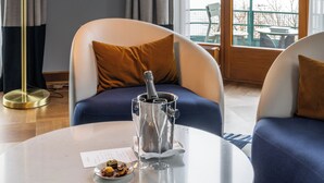 Ein modernes Hotelzimmer mit großem Fenster, einem runden Tisch, einer Champagnerflasche und zwei Sofas.