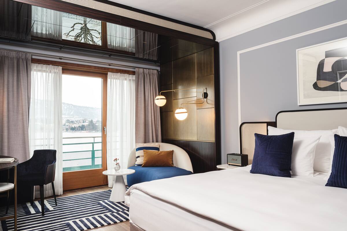 Habitación de hotel con cama, escritorio, silla, vistas al exterior y ventana con cortinas.