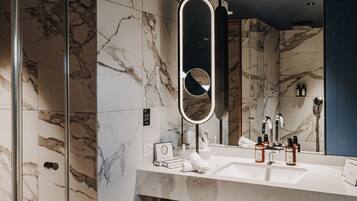 A modern bathroom with a marble wall, a large mirror, a sink, and toiletries.