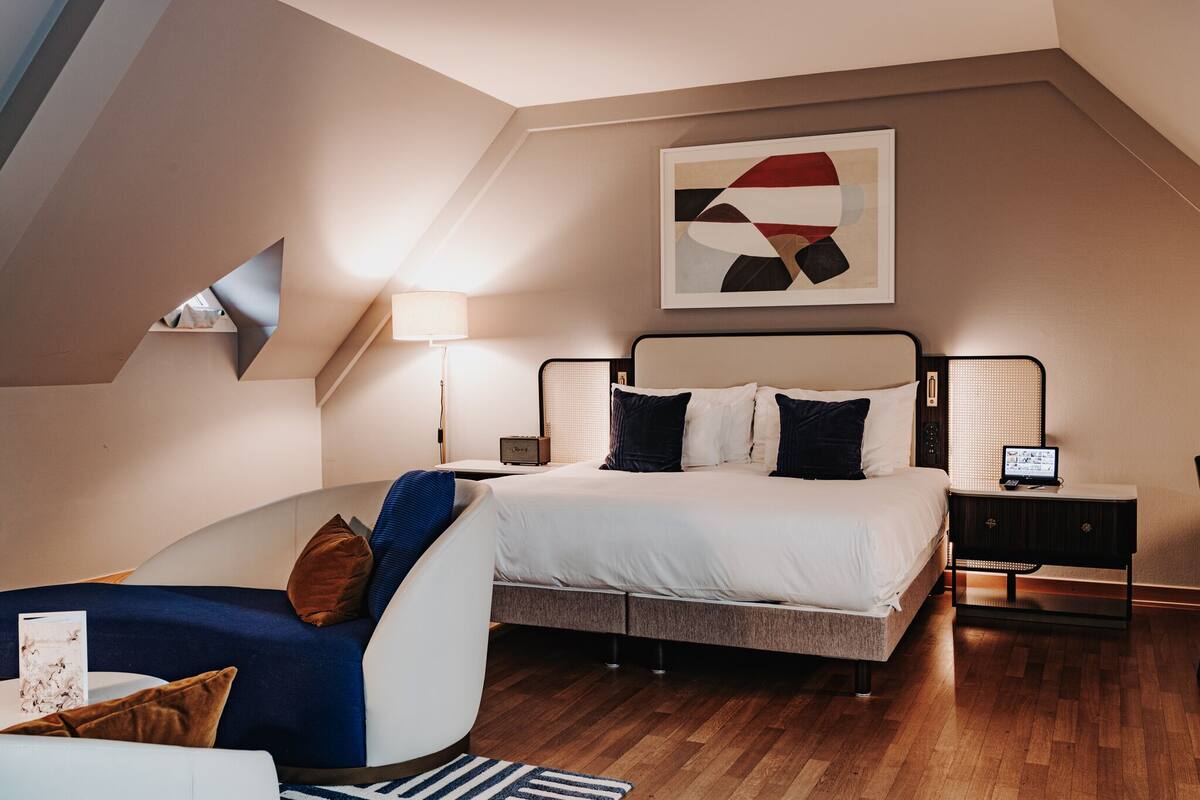 Un dormitorio moderno con cama, mesitas de noche, una lámpara y una obra de arte en la pared.