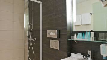 Un baño moderno con ducha envuelta en vidrio, inodoro blanco y un espejo grande sobre un lavamanos.