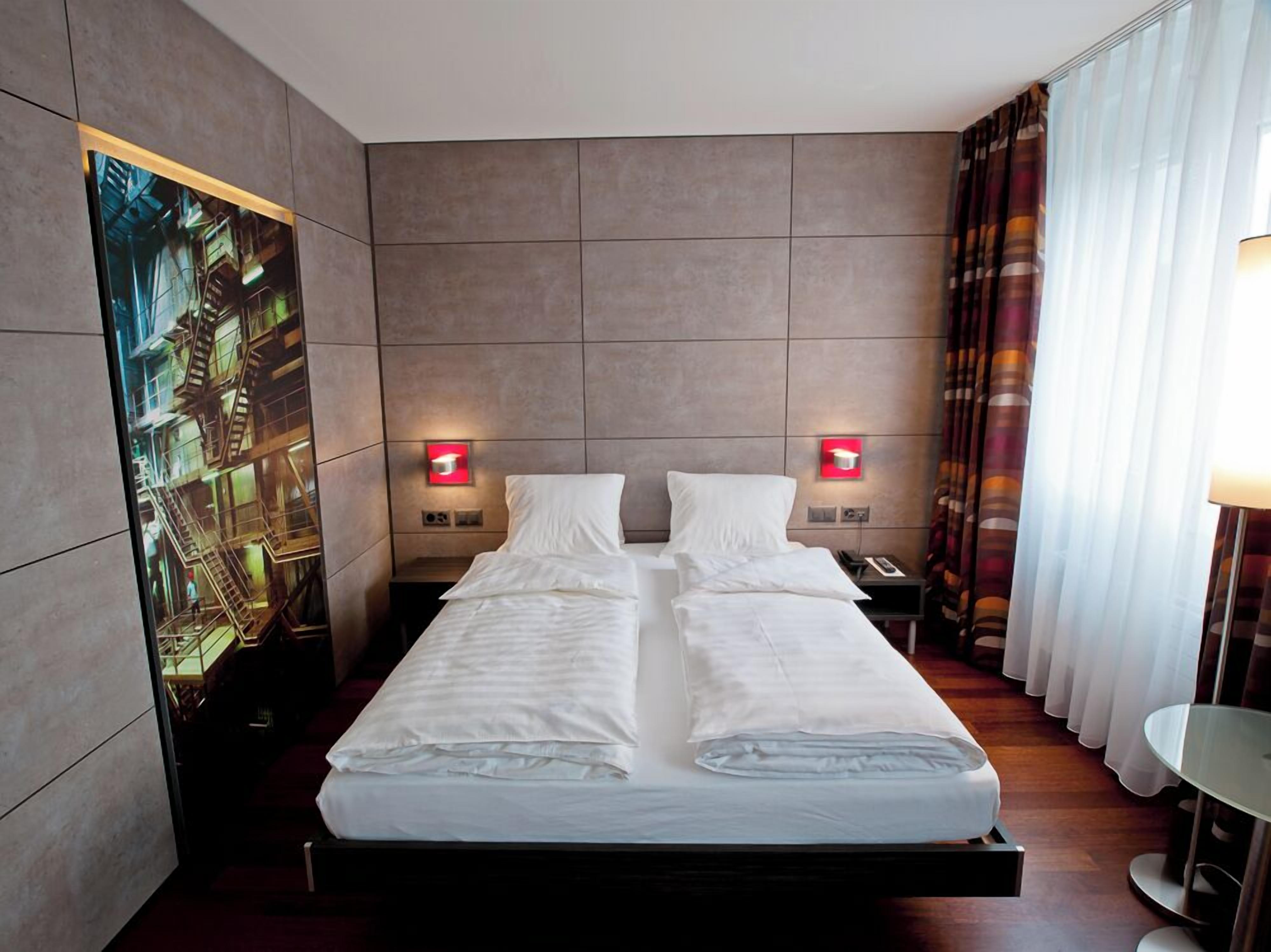 Ein modernes Hotelzimmer mit einem großen Bett, zwei Nachttischen und einem großen Fenster mit Vorhängen.