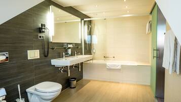 A modern bathroom with a large mirror, a sink, a toilet, and a bathtub.