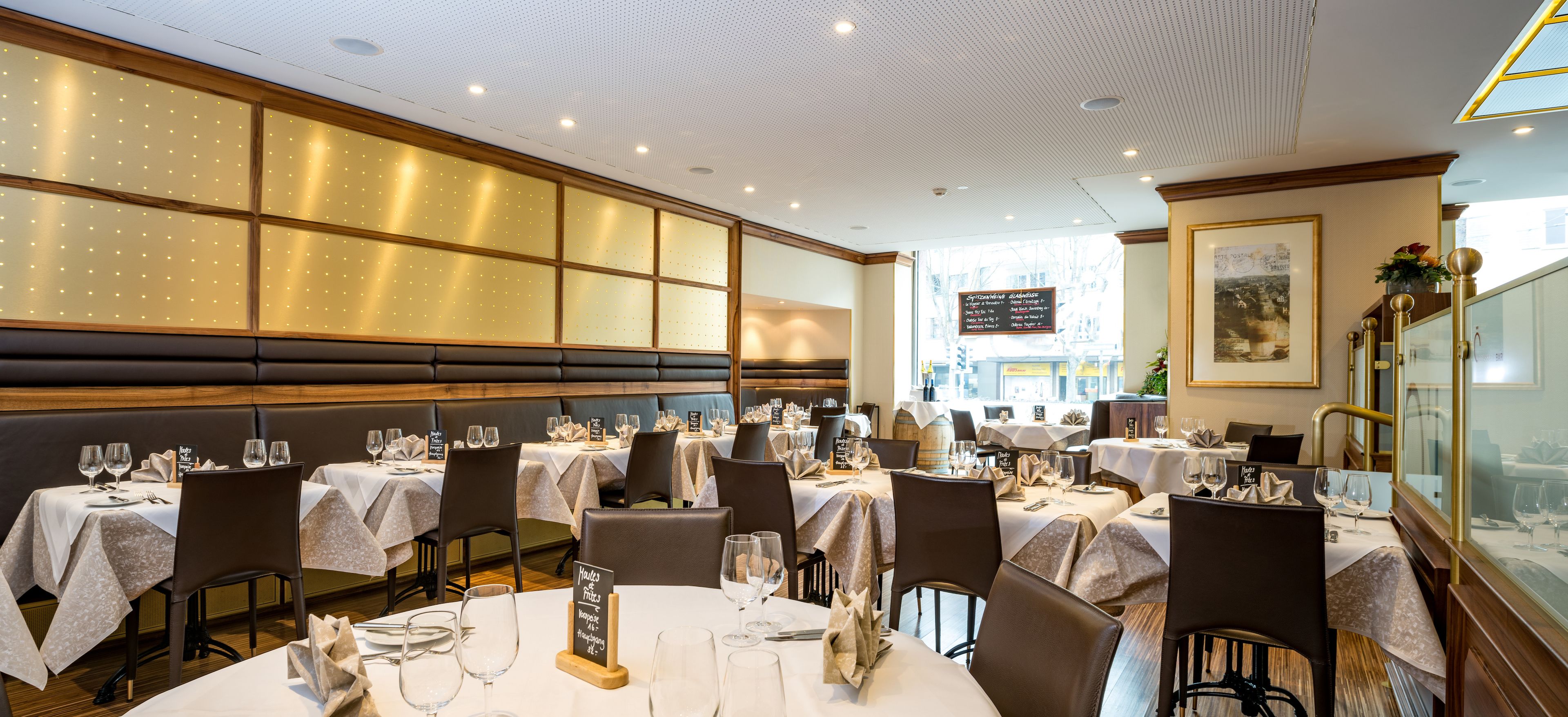 Un restaurant doté de nombreuses tables dressées pour le service, avec une disposition classique comprenant des banquettes et des tables rondes.