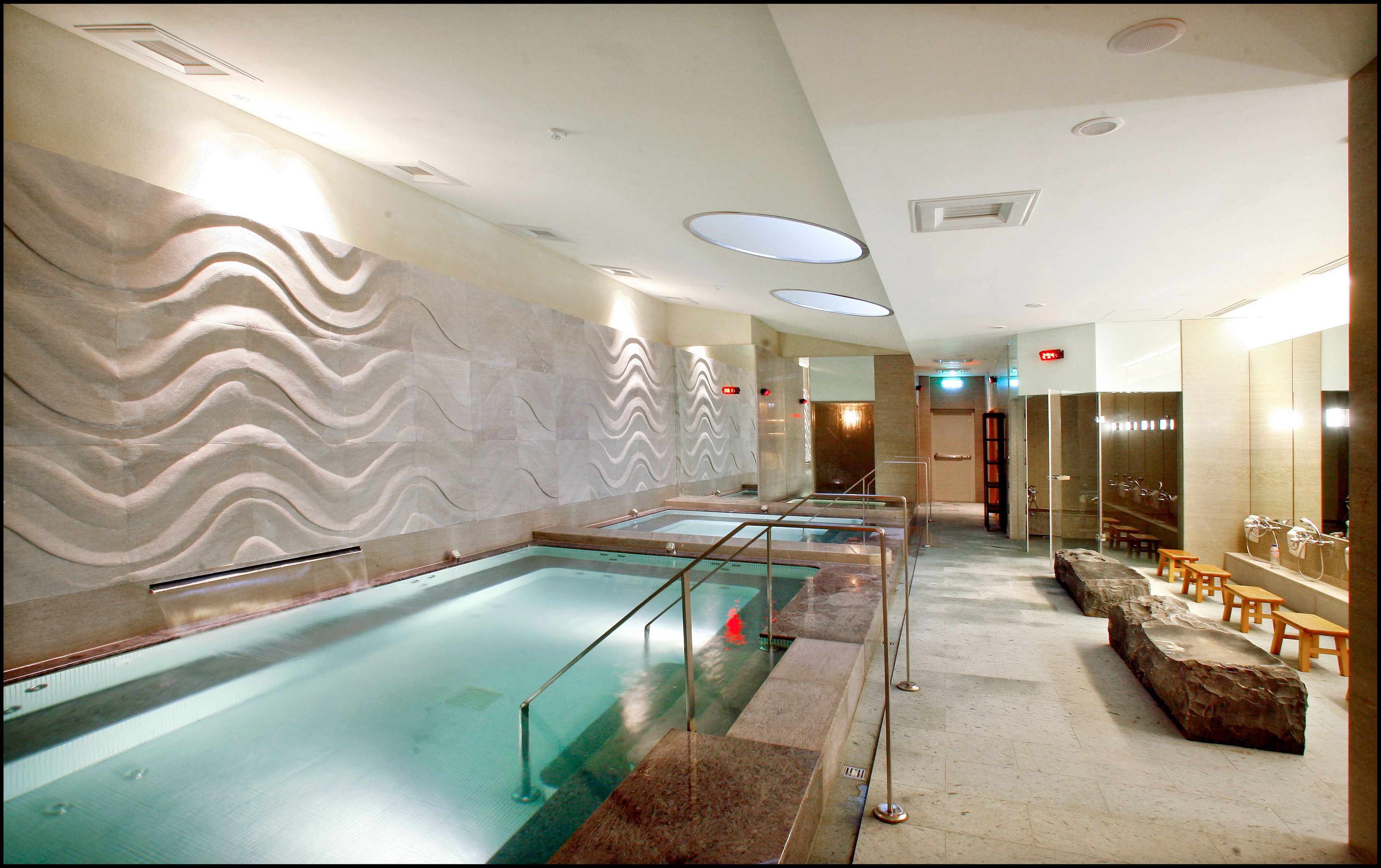 A spa area with multiple pools, a stone wall with a wavy pattern, and a seating area with wooden benches.