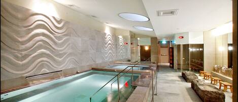 A spa area with multiple pools, a stone wall with a wavy pattern, and a seating area with wooden benches.