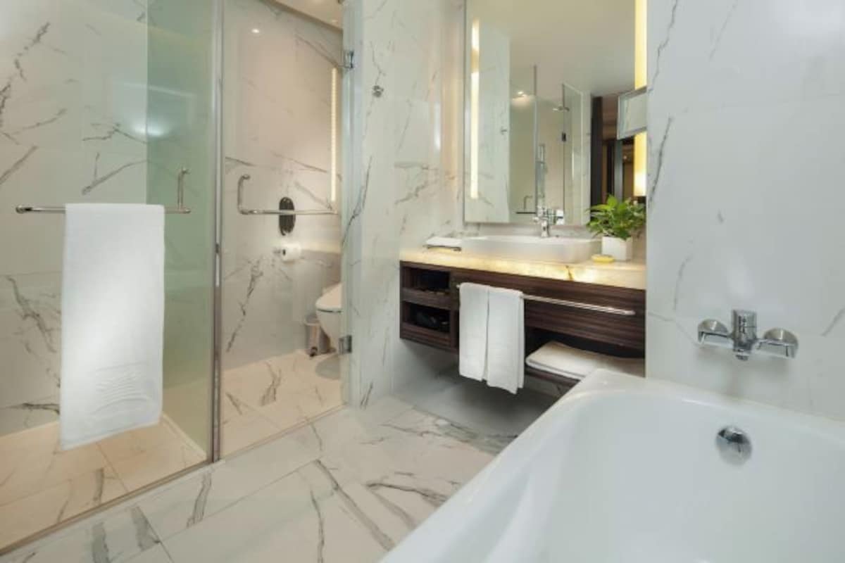 Een moderne badkamer met een glazen douchecabine, een marmeren vloer, een witte badkuip en een houten wastafelmeubel met een spiegel.