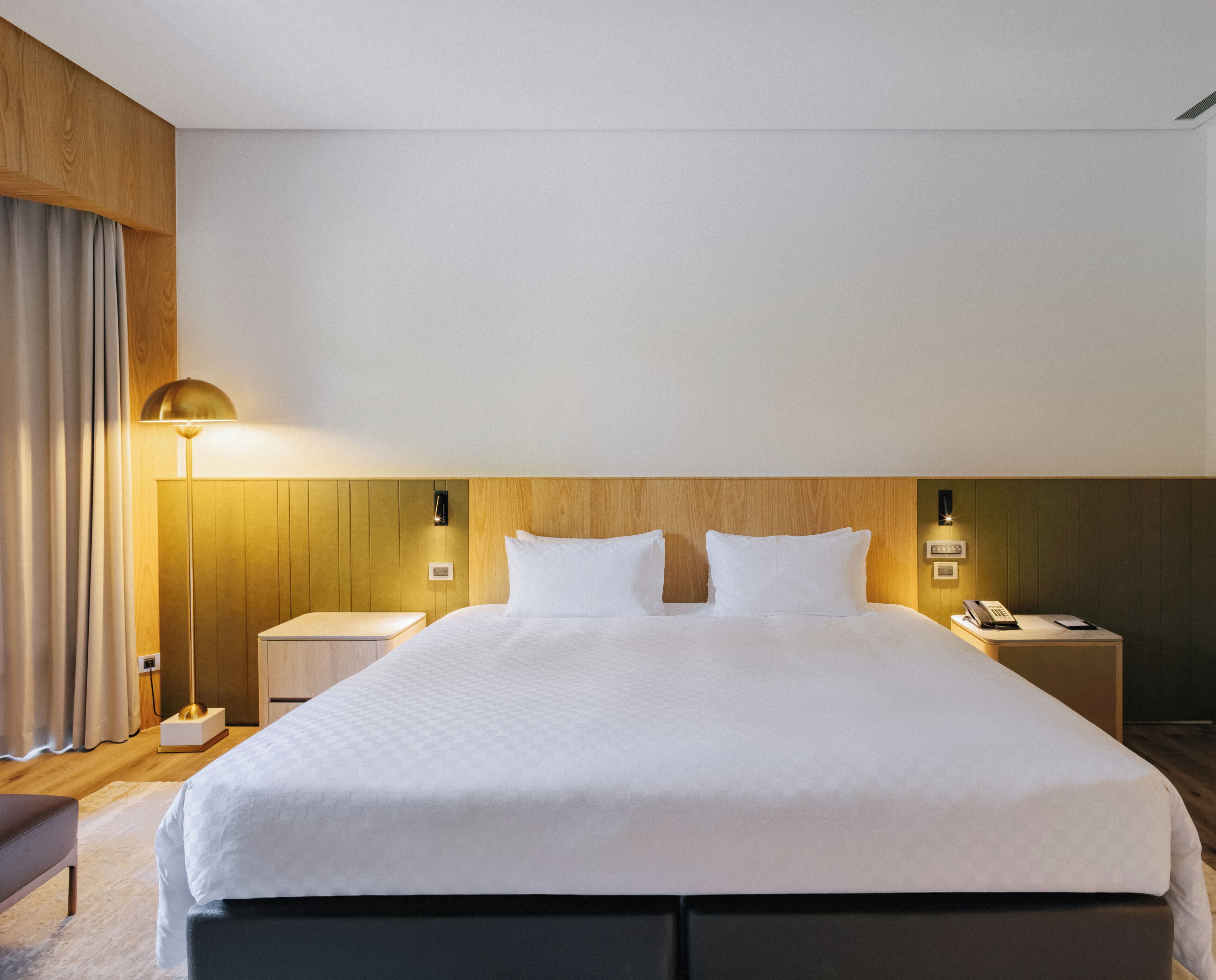 Een hotelkamer met een groot bed, nachtkastjes, een lamp en een telefoon.
