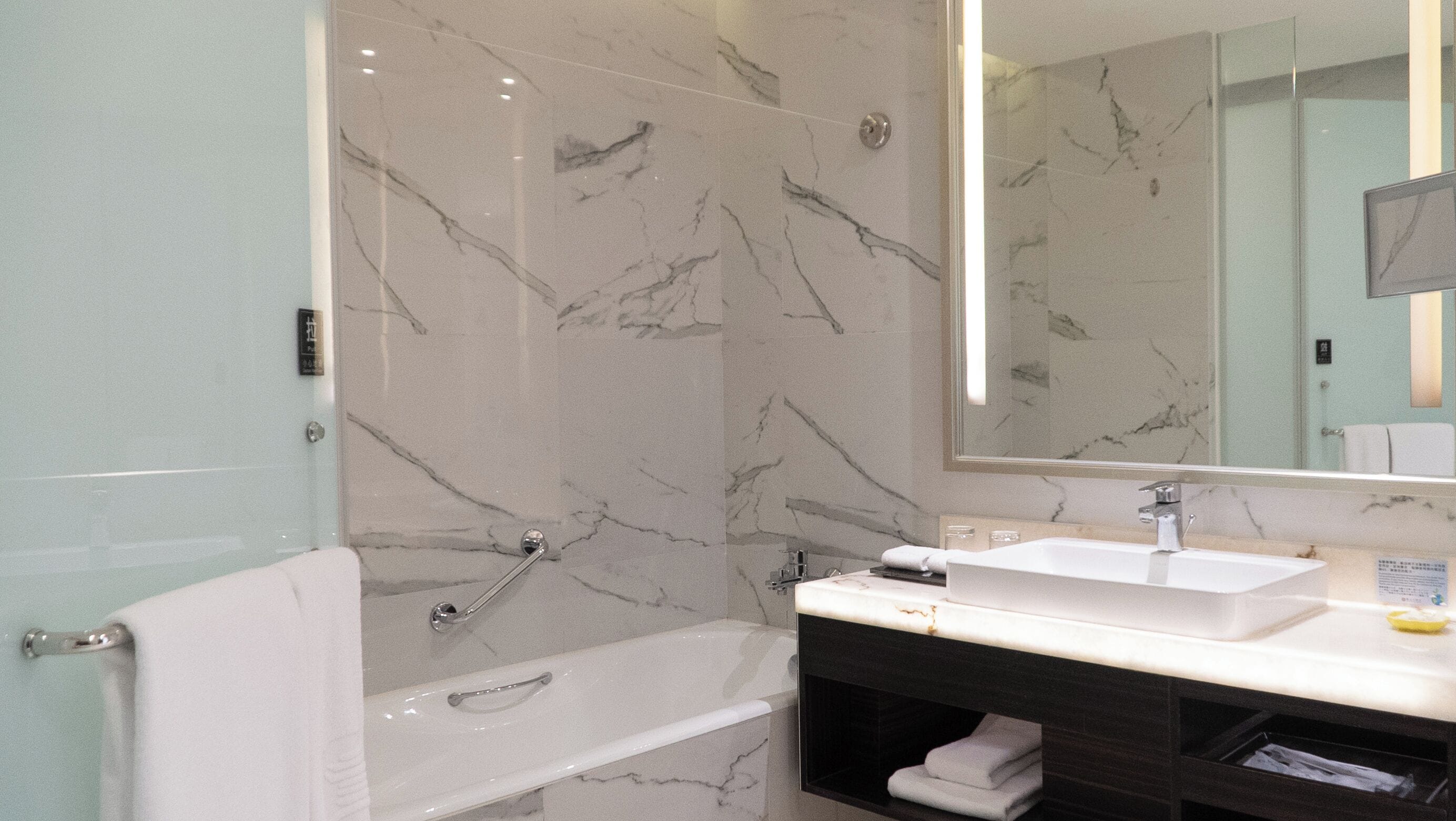A bathroom with a marble wall, a bathtub, a sink, and a vanity with a mirror.