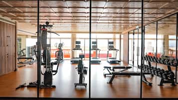 A gym with various exercise equipment, large windows, and a wooden floor.