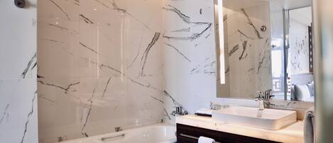 A modern bathroom with a marble wall, a bathtub, a vanity with a mirror, and a towel rack.