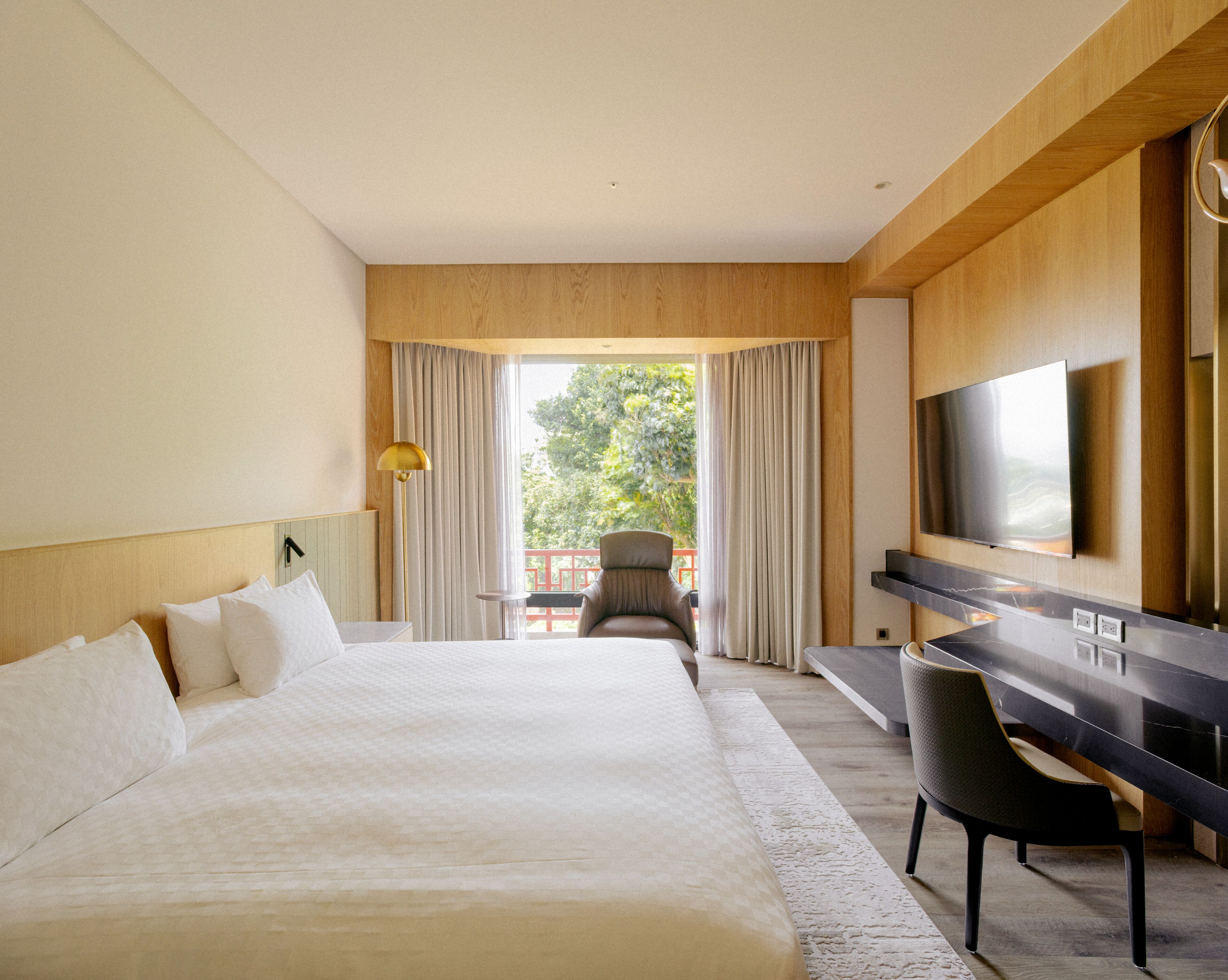 Habitación de hotel con una cama grande, un escritorio, una silla, un televisor y vistas al exterior.