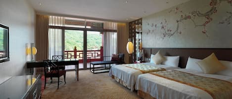 A hotel room with two beds, a desk, a chair, a TV, and a large window with a view of greenery.