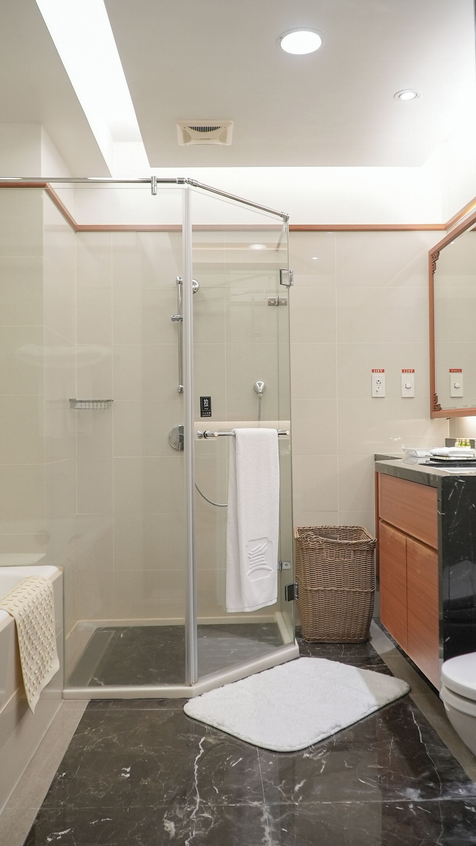 A modern bathroom with a glass shower enclosure, a vanity with a mirror, and a marble floor.