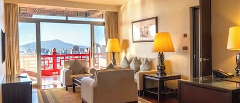 A hotel room with a large window, two lamps, a sofa, a coffee table, and a desk with a telephone.
