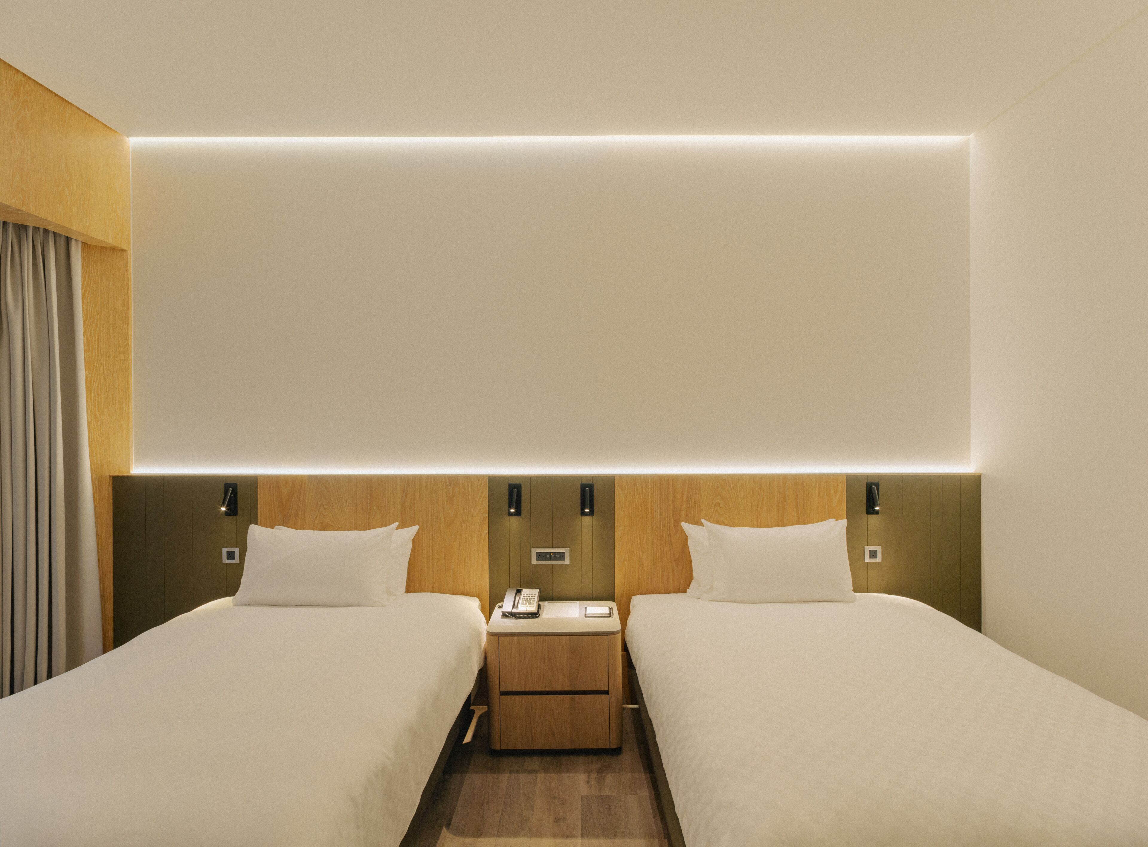 Una habitación de hotel con dos camas, una mesita de noche con teléfono y una lámpara fijada a la pared.