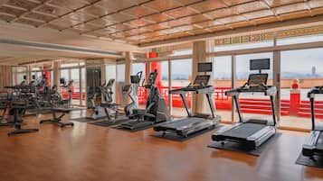 Une salle de sport spacieuse, équipée de divers appareils d’exercice, dotée de grandes fenêtres et offrant une vue sur le paysage urbain.