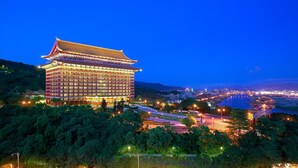A traditional-style hotel with a multi-story building, located near a river with a bridge in the background.