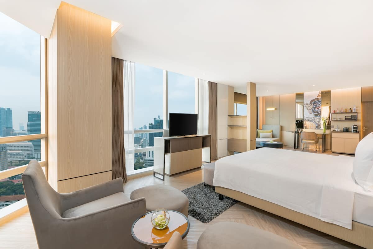 A modern hotel room with a large bed, a TV, a desk, and a view of the city.