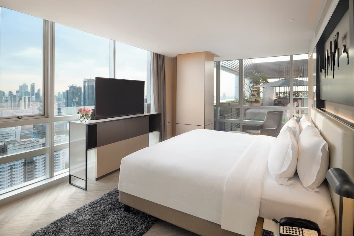 A modern hotel room with a large bed, a flat-screen TV, and a city view.
