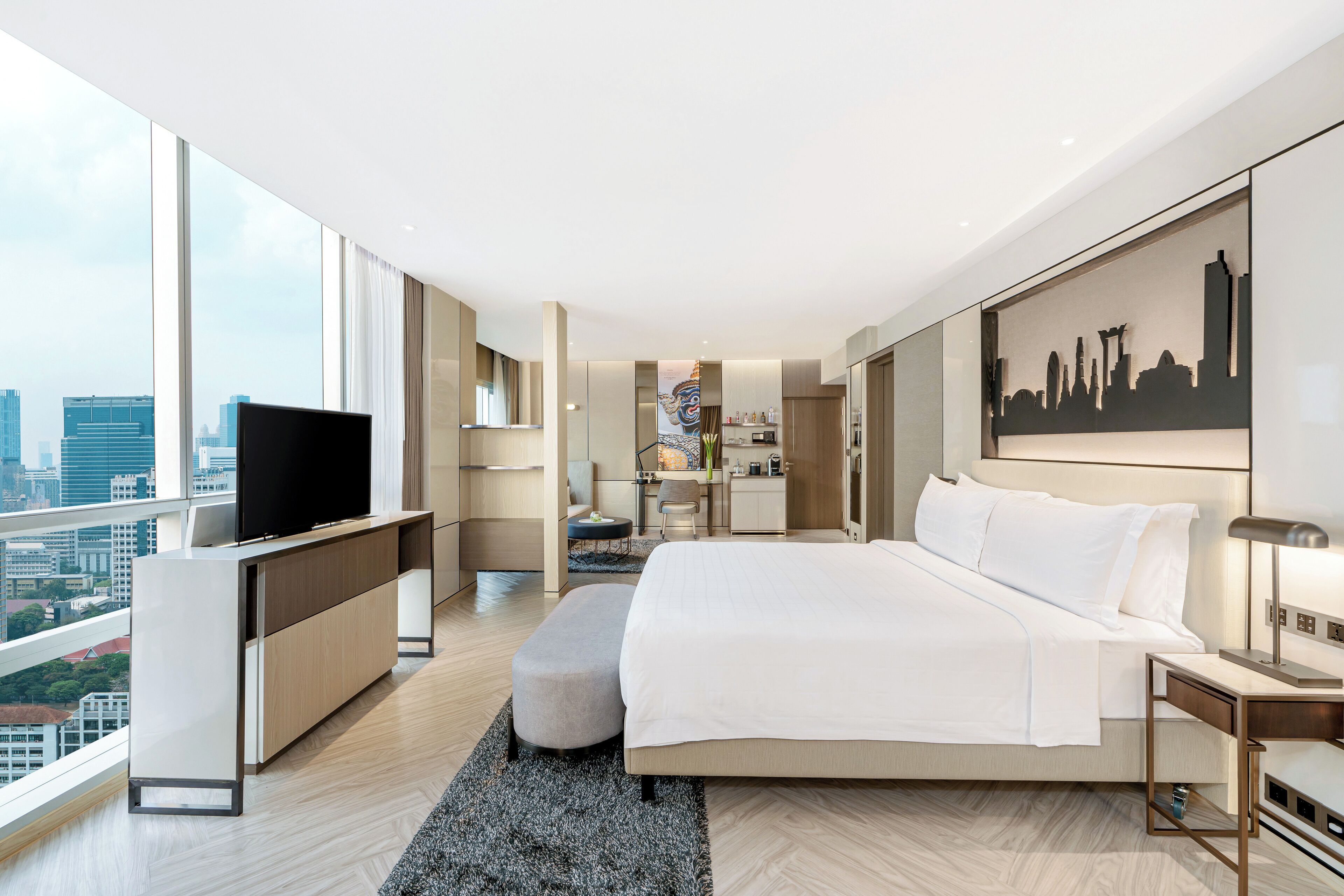 A modern hotel room with a large bed, a TV, a desk, and a city view.