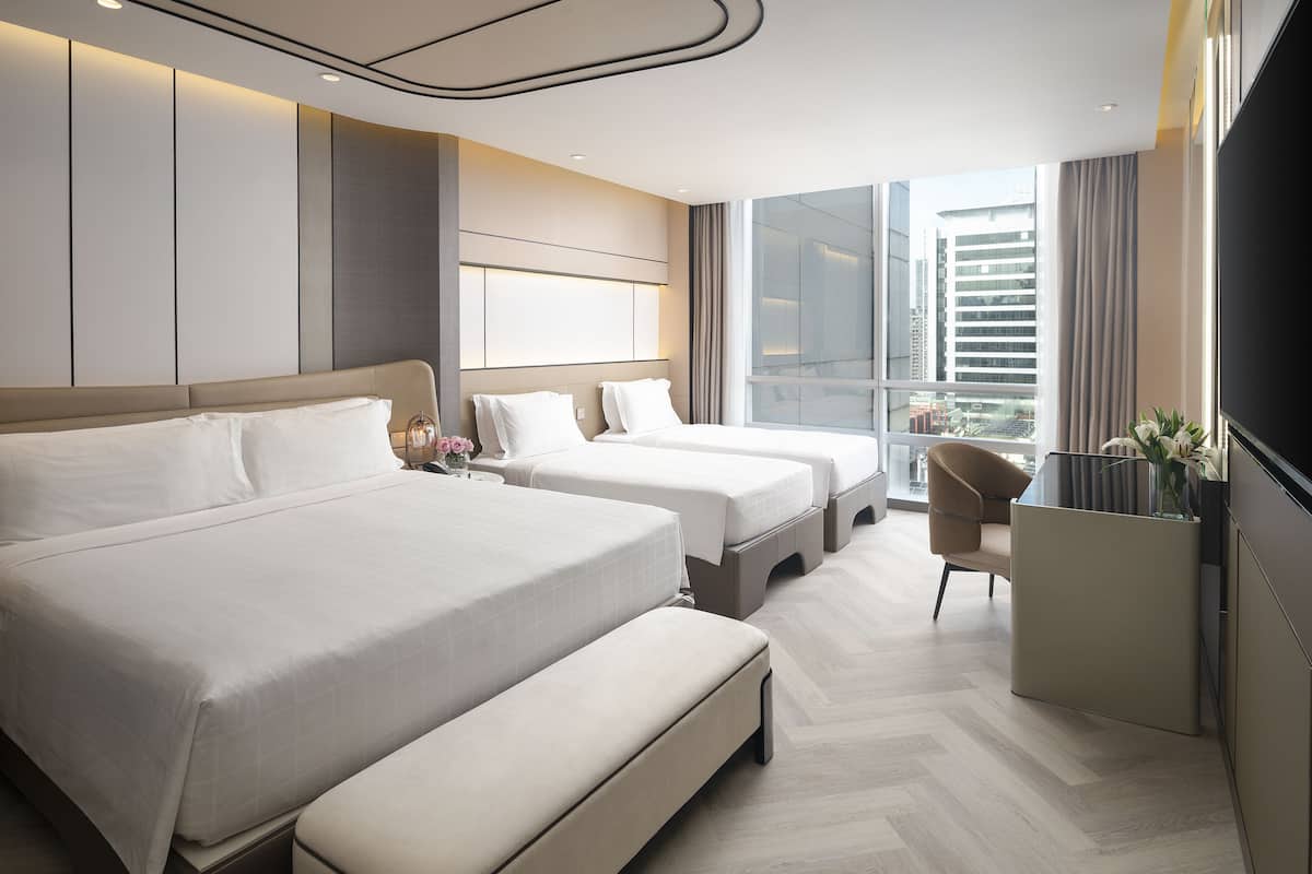 A hotel room with two beds, a desk, and a large window with a city view.