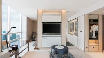 A modern hotel room with a large TV, a seating area with a coffee table, and a view of the city through large windows.