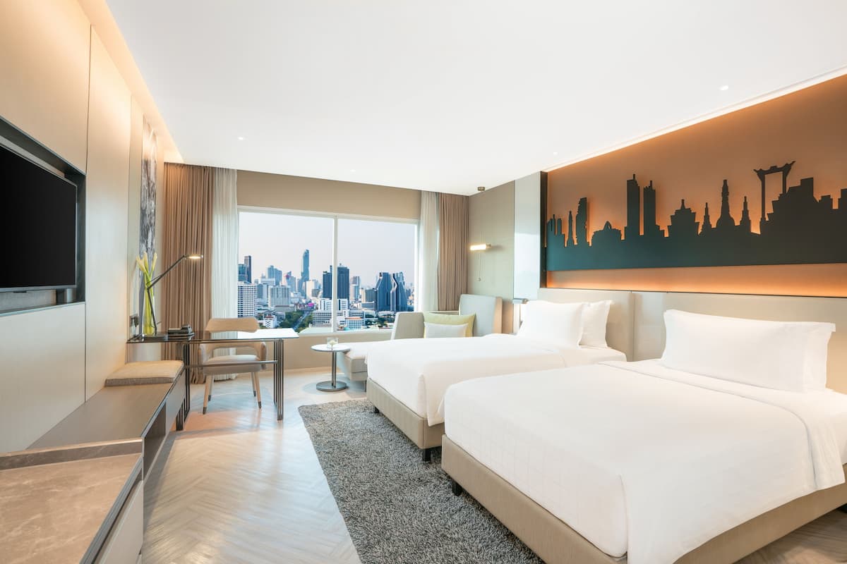 A hotel room with two beds, a city view, a flat-screen TV, and a city skyline artwork on the wall.