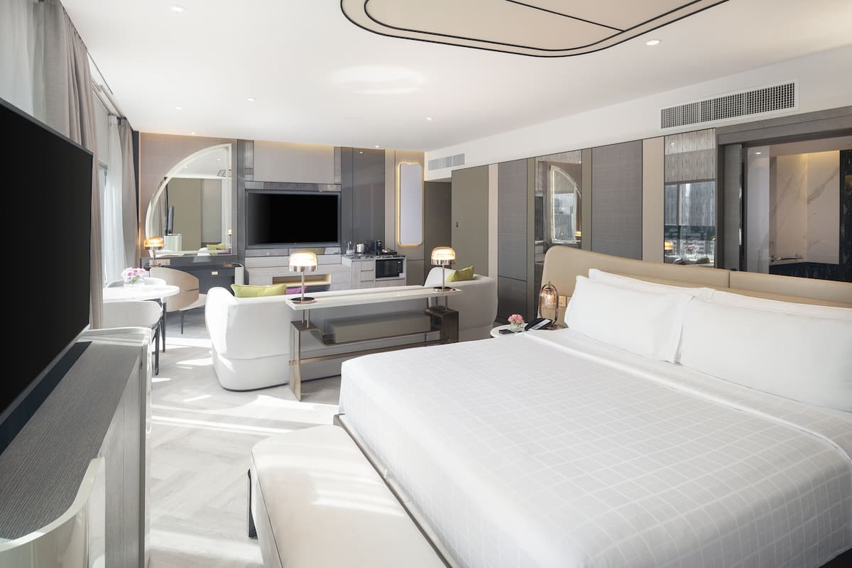 A modern hotel room with a large bed, a desk, a flat-screen TV, and a kitchenette.