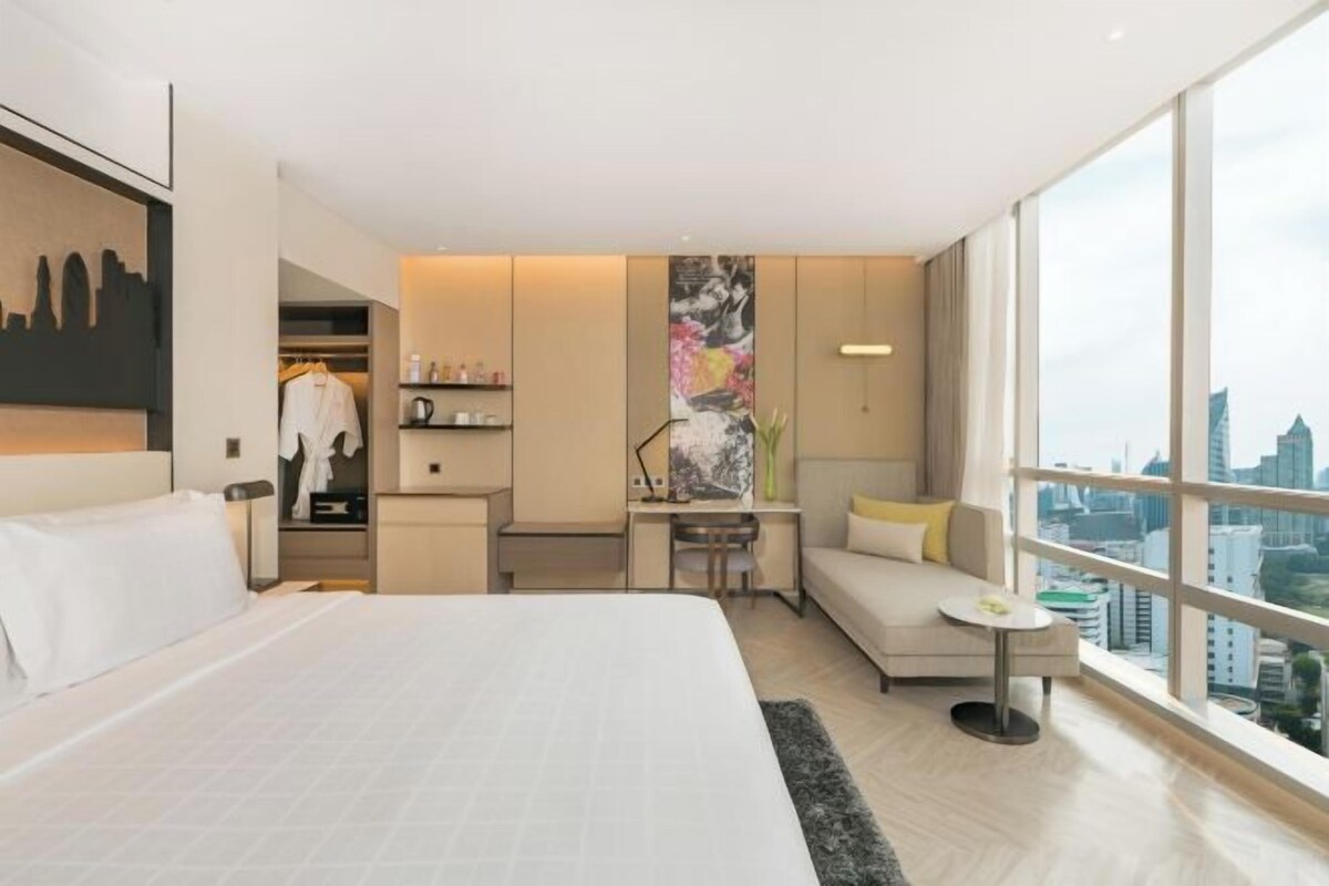 A modern hotel room with a large bed, a desk, a sofa, and a view of the city.